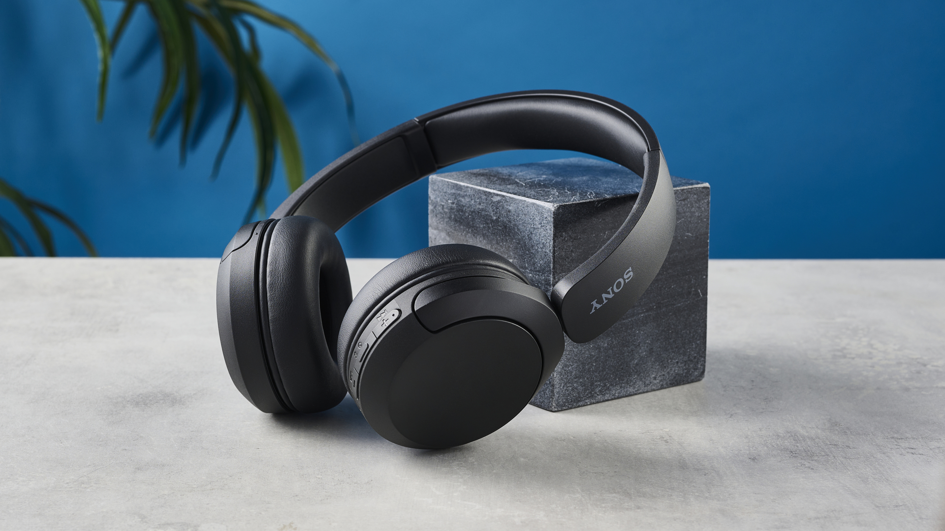 Een foto van de Sony WH-CH520 draadloze over-ear koptelefoons, rustend op een stenen oppervlak tegen een zwart marmeren blok en een blauwe achtergrond