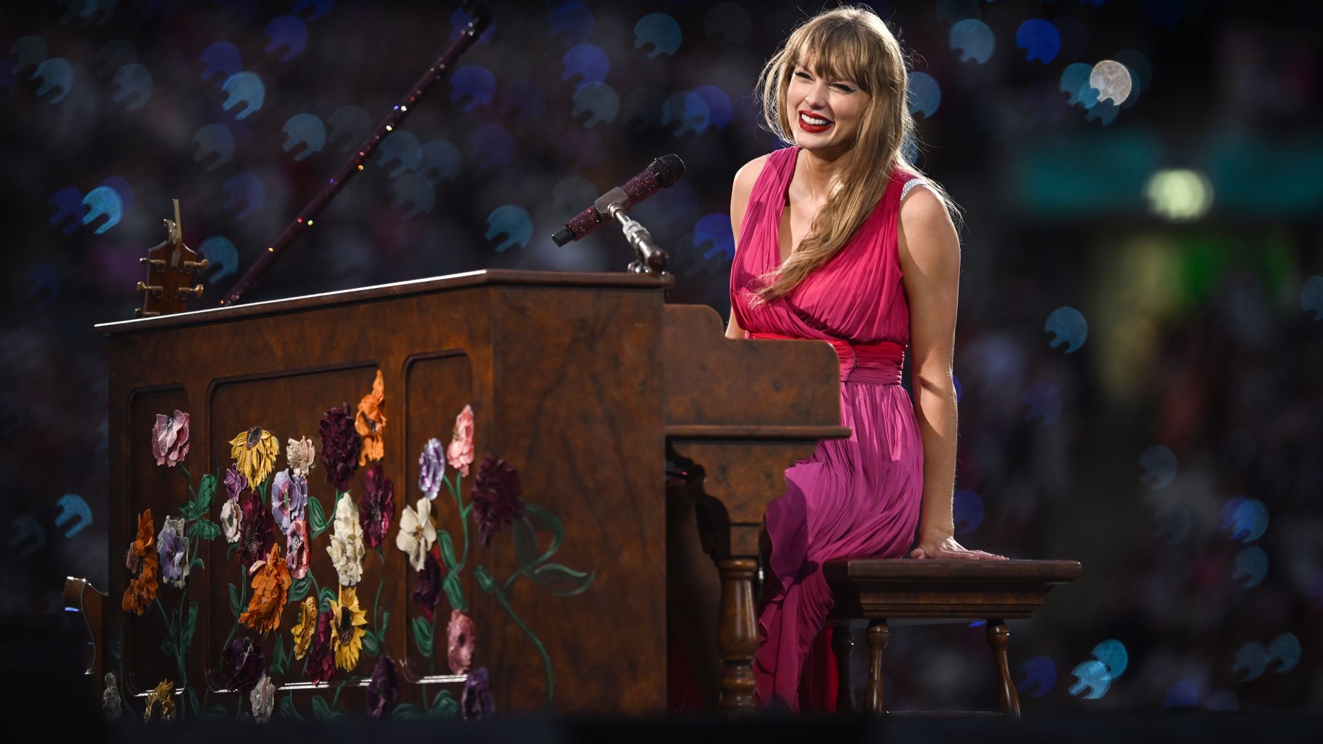 Taylor Swift op het podium in het Wembley Stadium op 23 juni 2024. Ze staat achter een met bloemen beschilderde piano en draagt een roze jurk