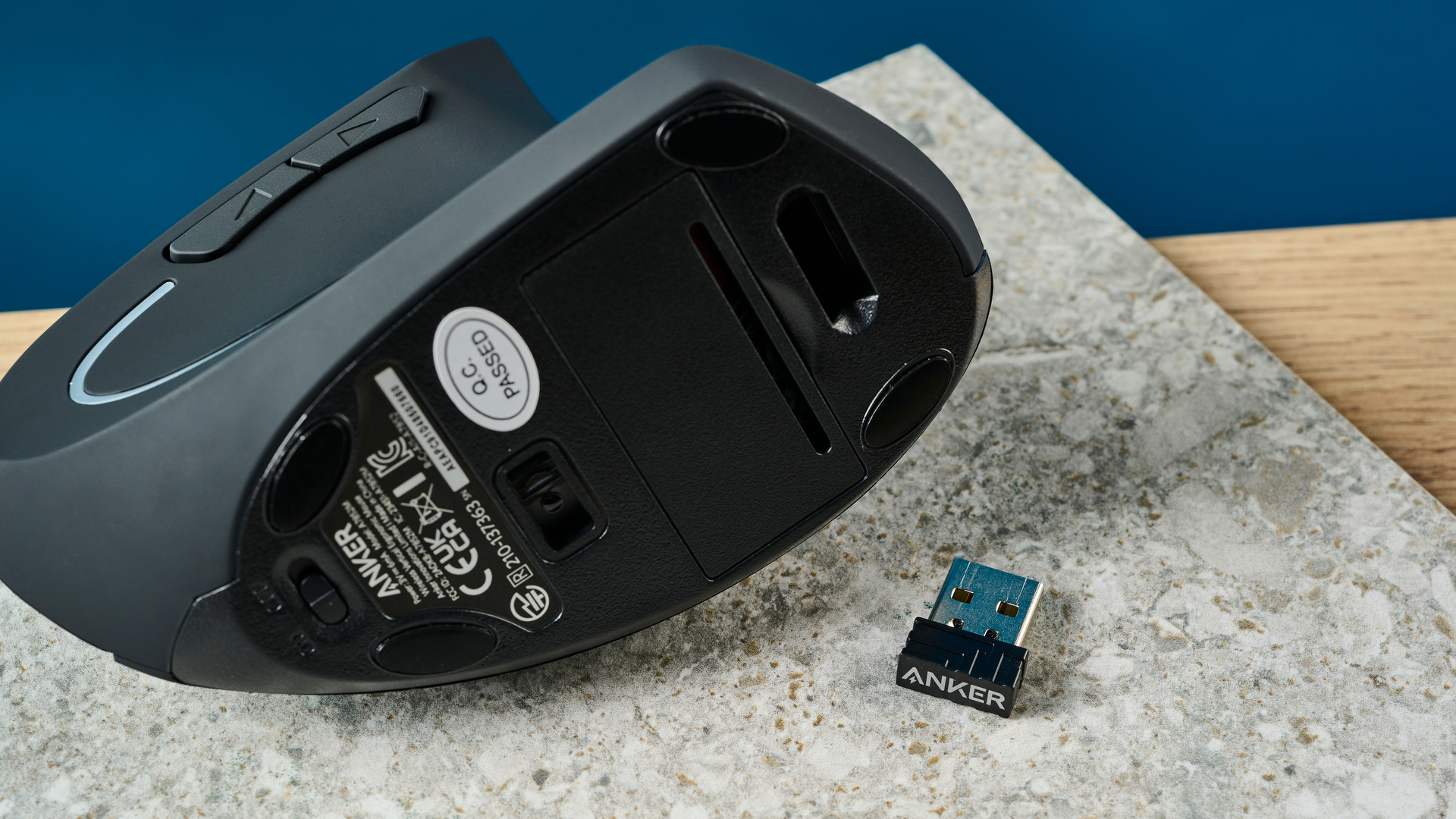 De Anker 2.4G Wireless Vertical Ergonomic Mouse op een stenen oppervlak met een blauwe muur op de achtergrond